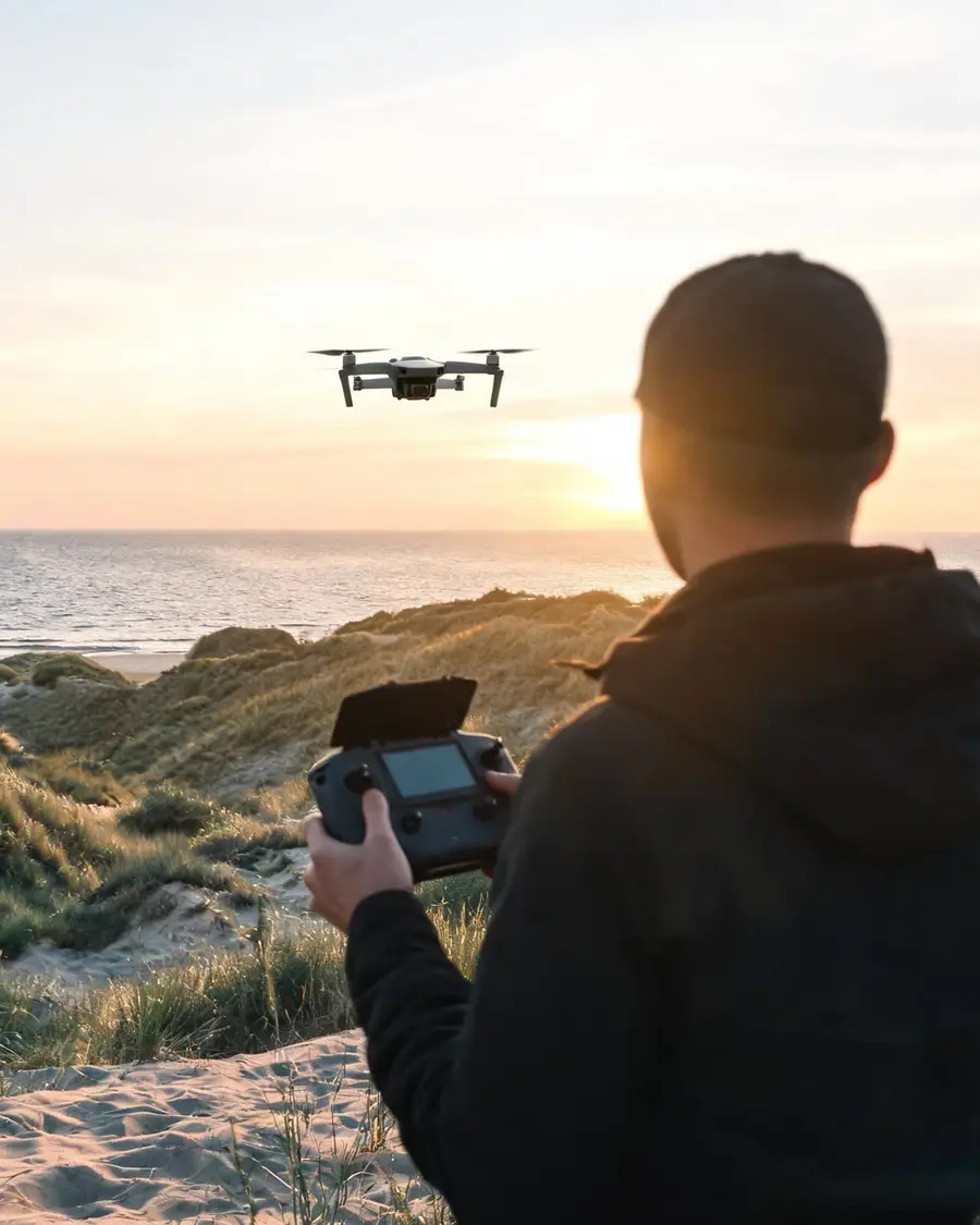 Operator drona na wydmie o wschodzie słońca, dron w powietrzu nad morzem